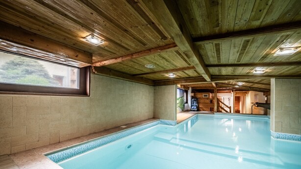 Une piscine intérieure avec des poutres en bois au plafond, des murs carrelés et une vue dégagée par une fenêtre.