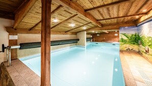 Une piscine intérieure avec des poutres en bois, un mur carrelé et une fresque murale.