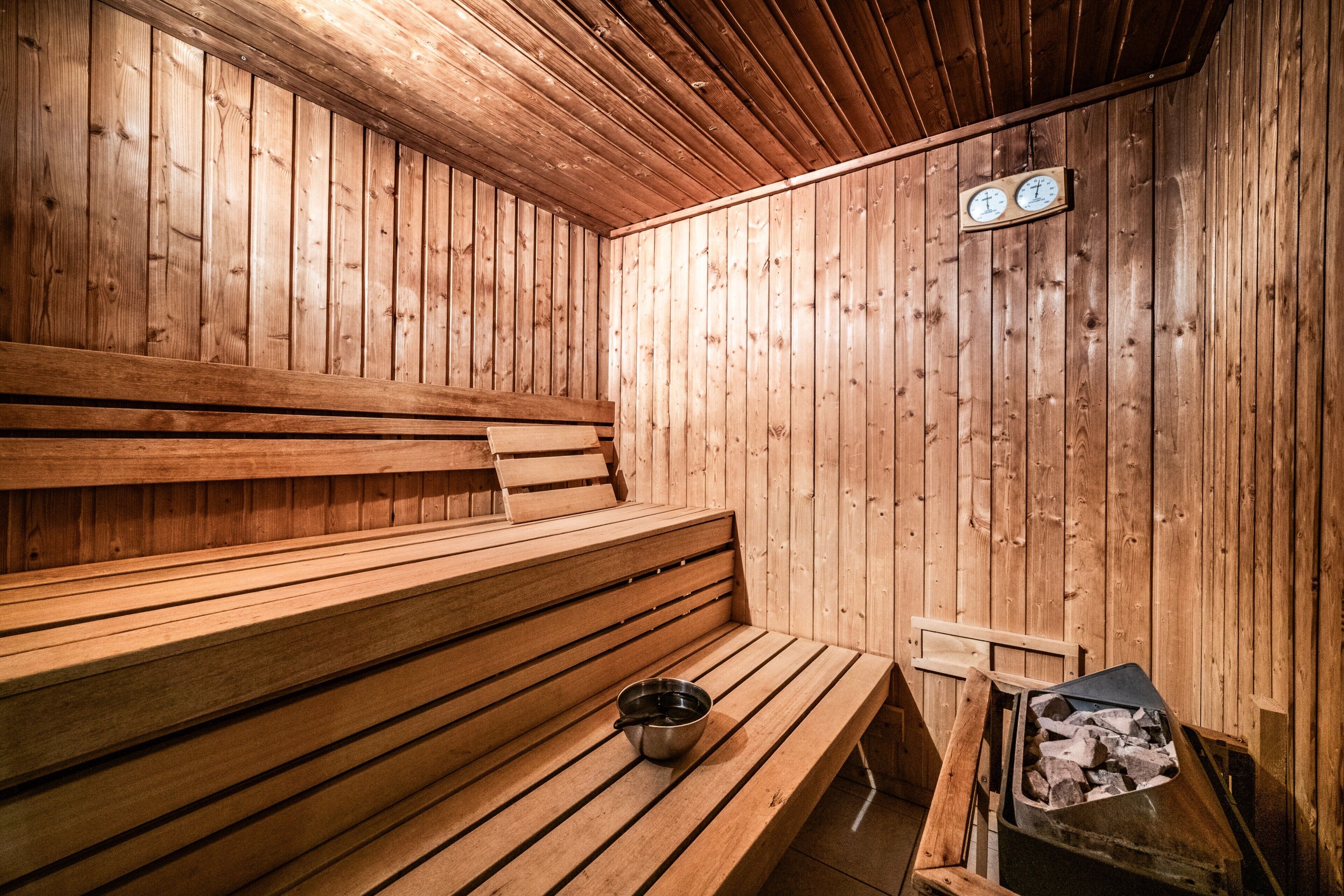 Una sauna de madera con bancos, un balde y un horno de leña.