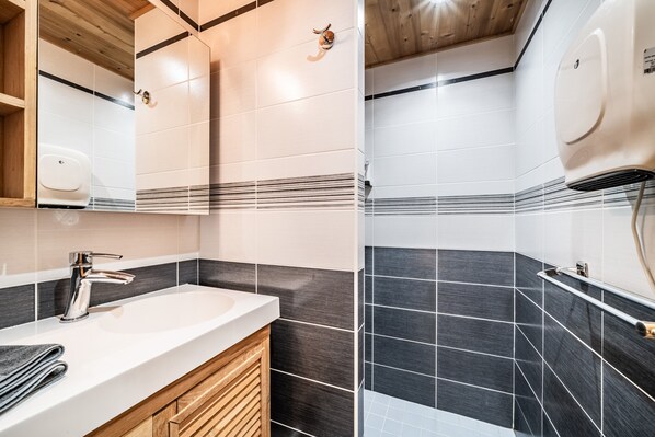 A modern bathroom with a white sink, wooden vanity, and black and white tiled walls.