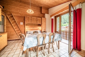 Un intérieur en bois comprenant une table à manger, des chaises, une échelle et une vue à travers une porte vitrée.