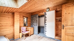 A wooden cabin interior with a bed, a chair, a desk, a stone fireplace, and a wardrobe. - Apartment 'Le Chamois De Vermeil - 6 People' with Mountain View, Balcony and Wi-Fi (Châtel)
