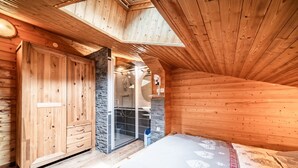 Una cabaña de madera con un dormitorio en el altillo, una pared de piedra y una zona de ducha.