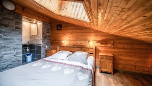 Ein Schlafzimmer mit Holzboden, einer Steinwand, einem Bett mit Bettwäsche mit Herzmuster, einem Nachttisch und einem Badezimmer mit Waschbecken und Spiegel.