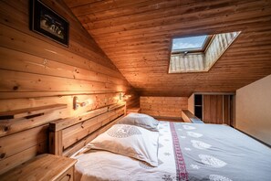 Une chambre dans une cabane en bois, dotée d’un puits de lumière, d’un lit avec une literie à motifs et d’un luminaire fixé au mur.