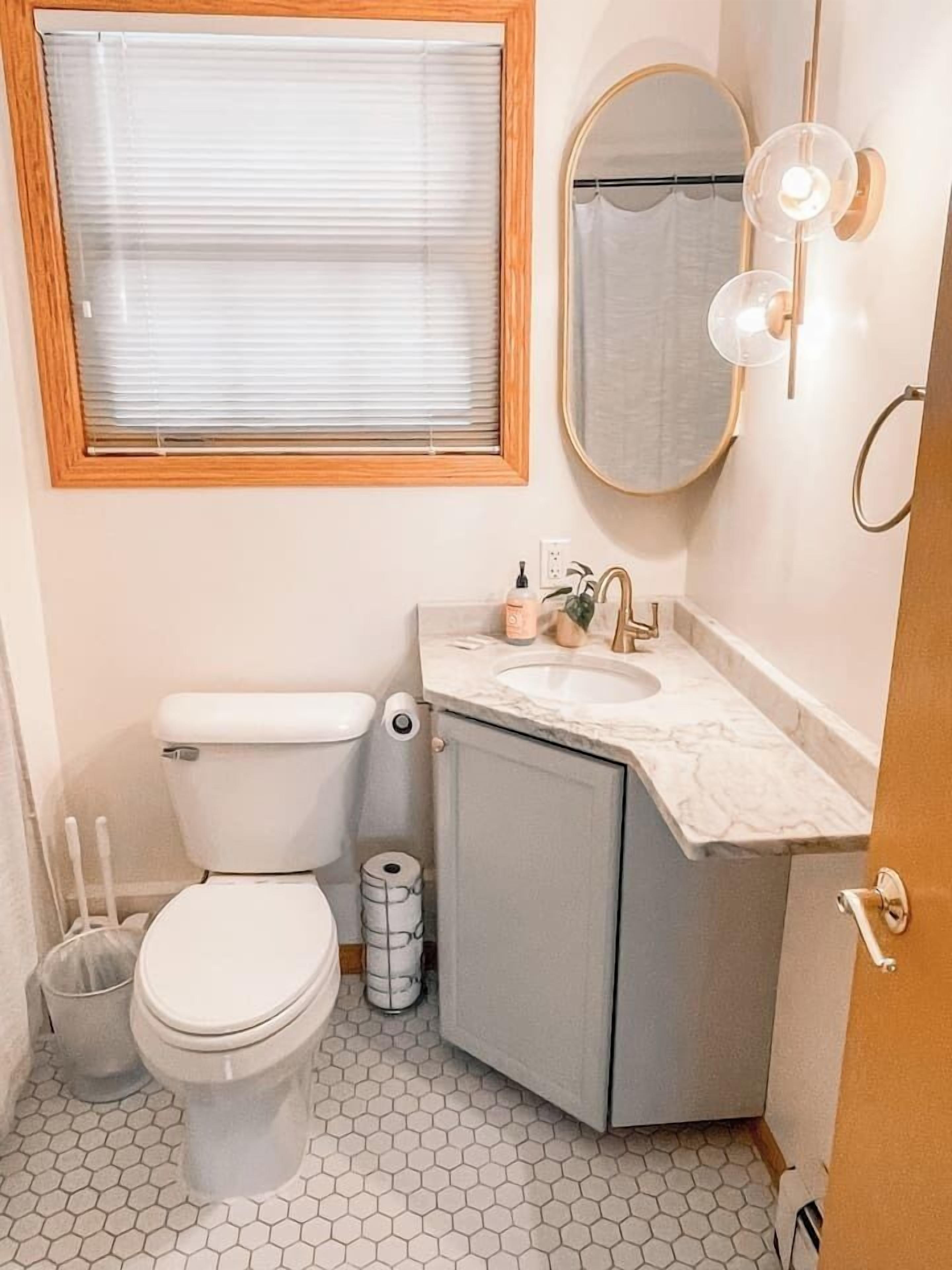 Un baño con inodoro, lavabo, espejo y una ventana con persianas.