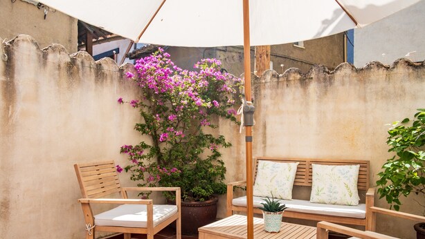 Une terrasse extérieure avec des meubles en bois, une plante en pot et un parasol blanc.