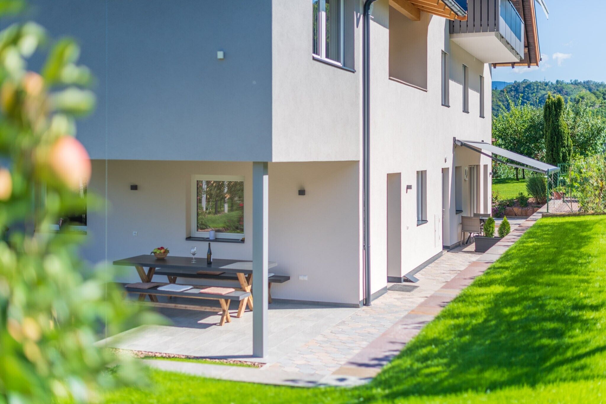 Ein modernes, zweistöckiges Haus mit einer Terrasse, Sitzgelegenheiten im Freien und einem gepflegten Rasen.