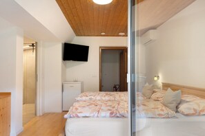 A bedroom with a wooden ceiling, a bed with patterned bedding, a television on the wall, and a small refrigerator. - Room 'Haus Stolz  with Breakfast' with Mountain View, Wi-Fi and Air Conditioning (Unterrain/Eppan a. d. Weinst)