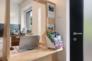 A hotel reception desk with a computer, a magazine rack, and a door to the right.