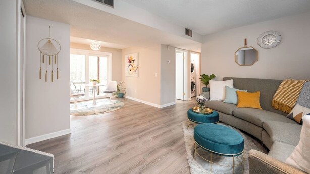 A spacious living room with a grey sofa, teal ottoman, and a coffee table. A dining area is visible in the background with a round table and chairs. - Pets~Trails~Beaches~10mins to TC~2 Person Suite (Williamsburg)