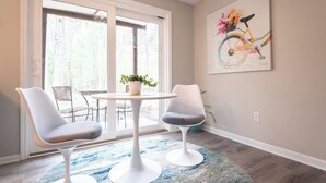 A room with a round table, two chairs, a potted plant, and a painting of a bicycle. - Pets~Trails~Beaches~10mins to TC~2 Person Suite (Williamsburg)