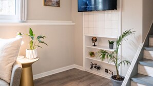 A modern living room with a flat-screen TV mounted on the wall, a staircase, and a potted plant. - Pets~Trails~Beaches~10mins to TC~2 Person Suite (Williamsburg)