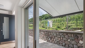 Un interior moderno con un amplio ventanal corredero que da a un espacio exterior con un muro de piedra y vistas a un viñedo.