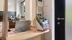 A hotel reception desk with a computer, a magazine rack, and a door to the right.