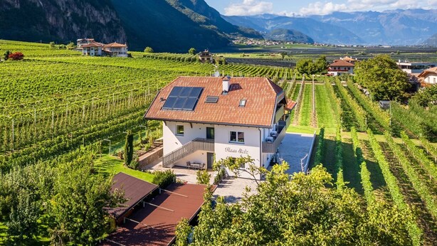 A house with a red roof, solar panels, and a vineyard in the background.