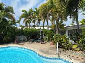 Relax by the serene pool surrounded by lush tropical vegetation and a white picket fence.
