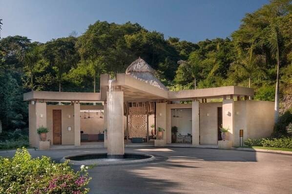 A modern building with a central water feature, surrounded by lush greenery.