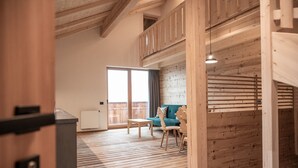 A spacious room with a wooden floor, a sofa, a table, and a balcony with a view.
