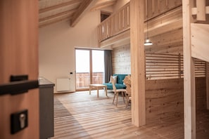 A spacious room with a wooden floor, a sofa, a table, and a balcony with a view.