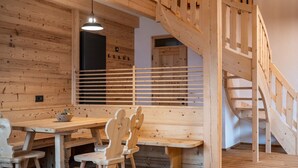 A wooden interior with a staircase, a table with chairs, and a hanging light fixture.