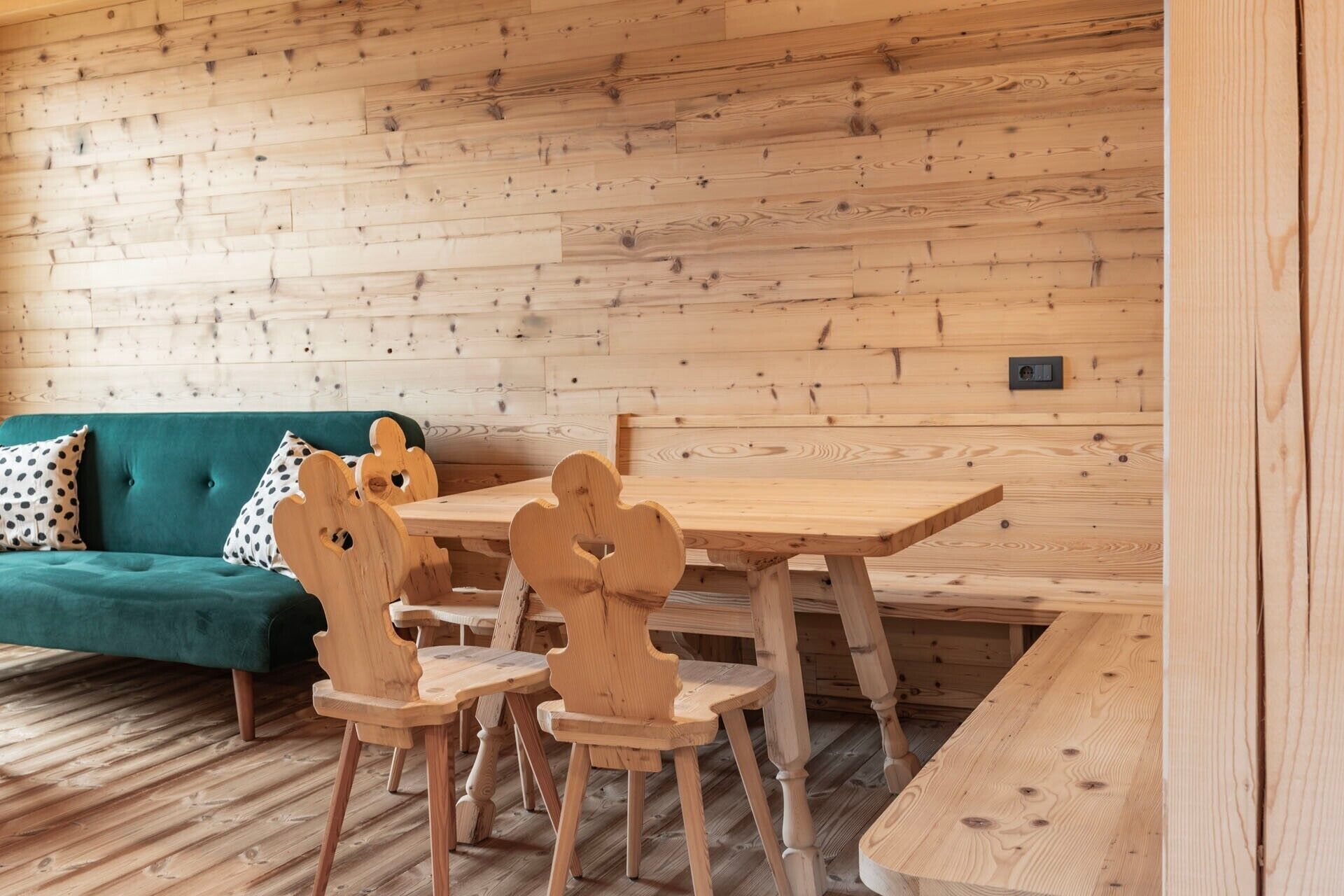 A wooden interior with a green sofa, wooden chairs, and a wooden table.