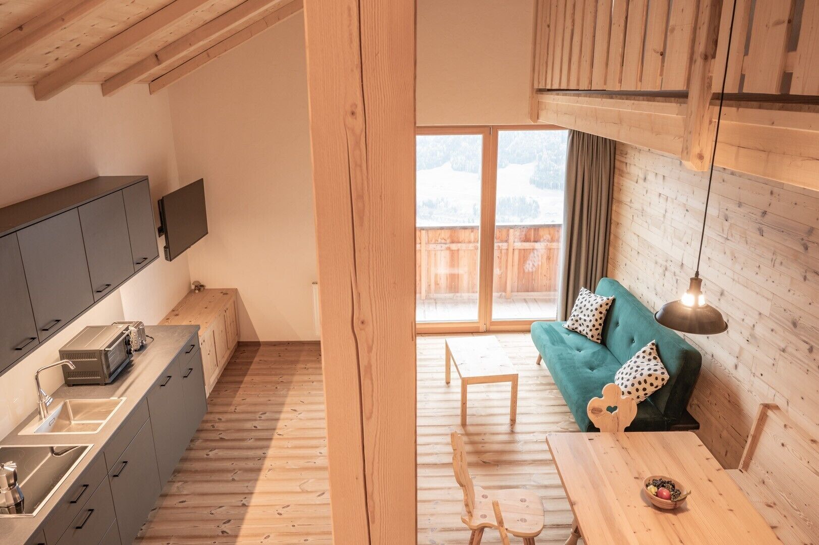 A compact kitchen with modern appliances, a dining area with a wooden table and chairs, and a cozy seating area with a sofa and cushions.
