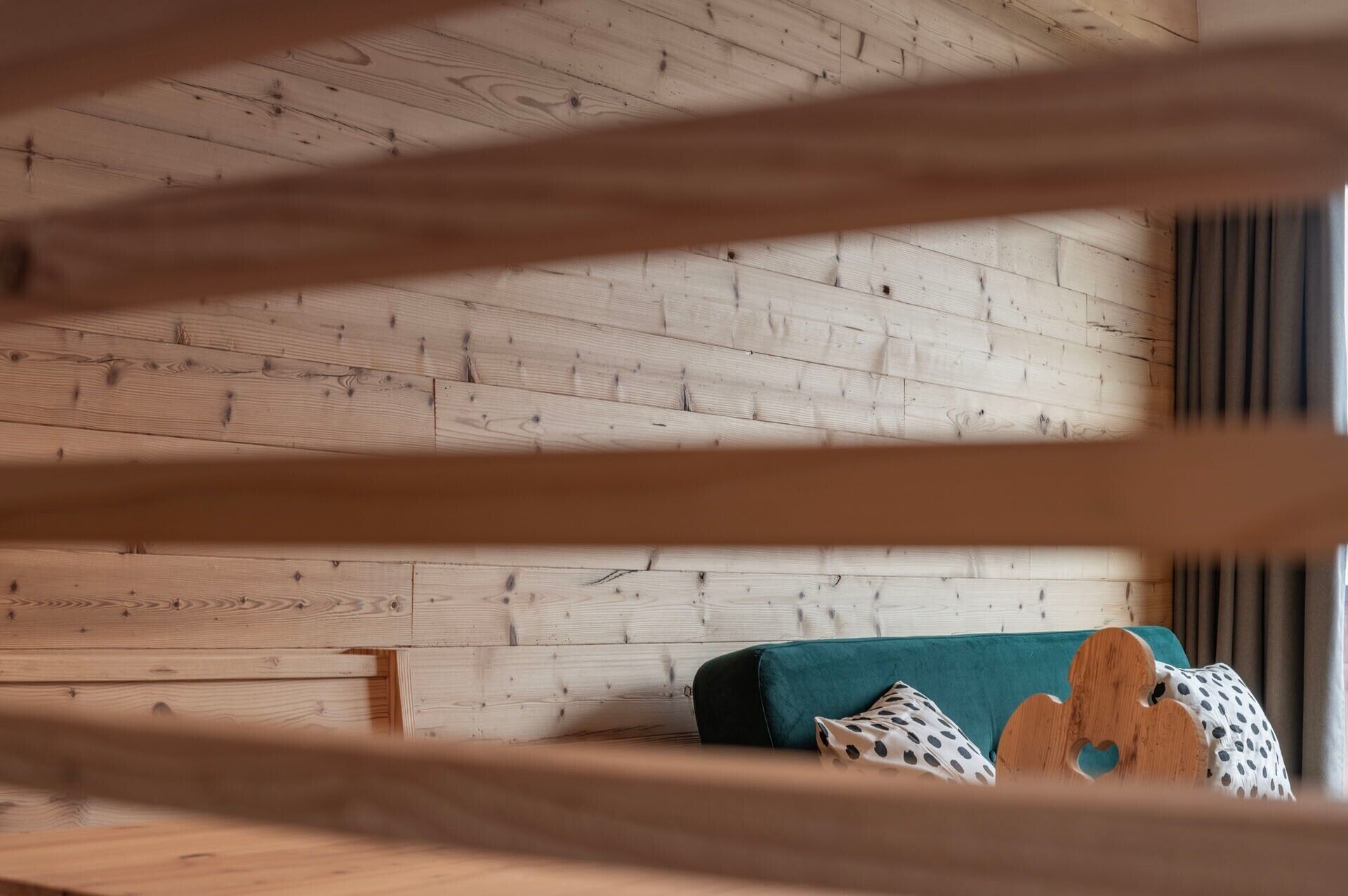 A room with wooden walls and a teal sofa with patterned cushions.