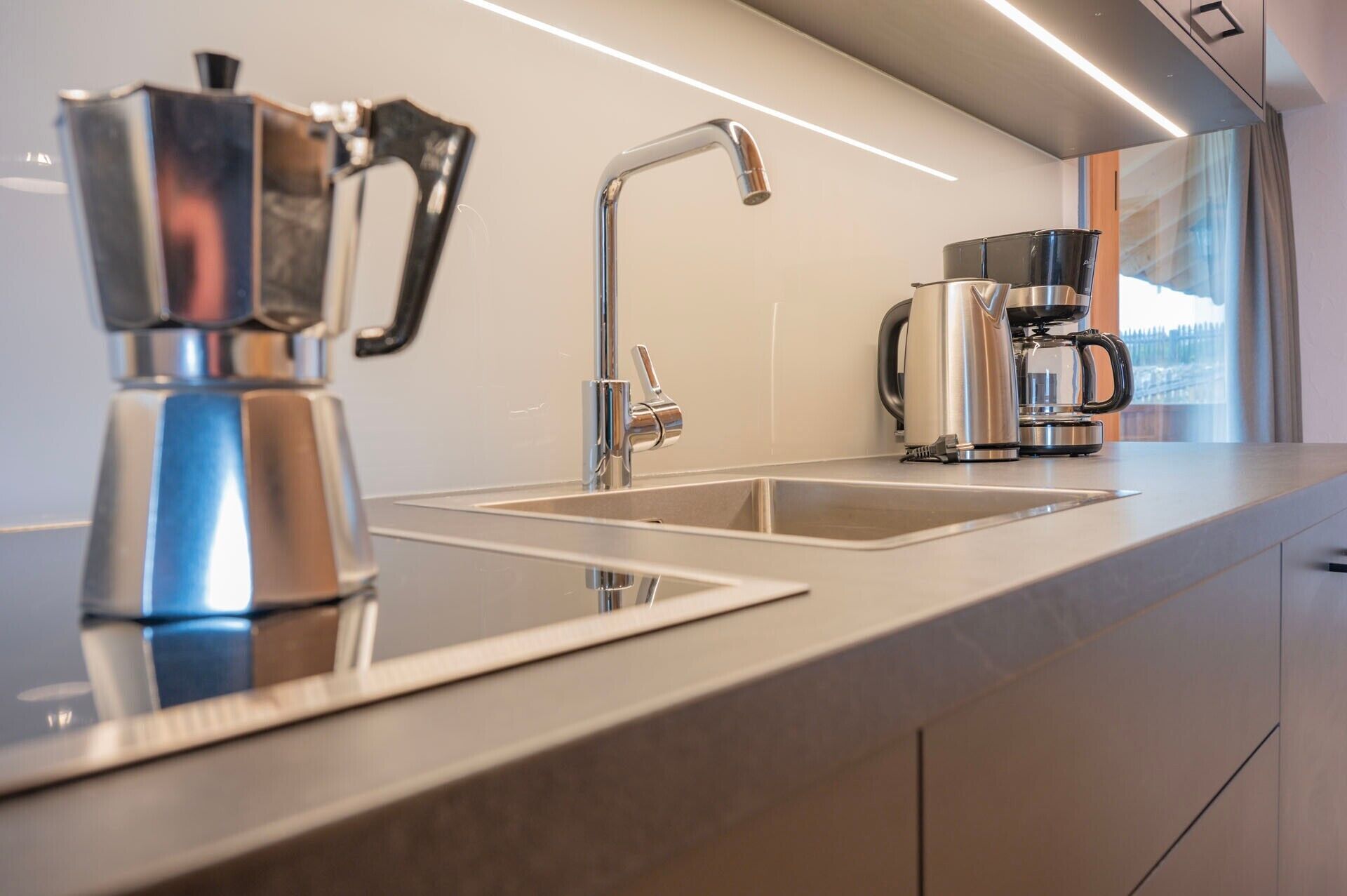 Et moderne køkken med en stål kaffemaskine, en hanefaucet og en kaffepotte på bordpladen.