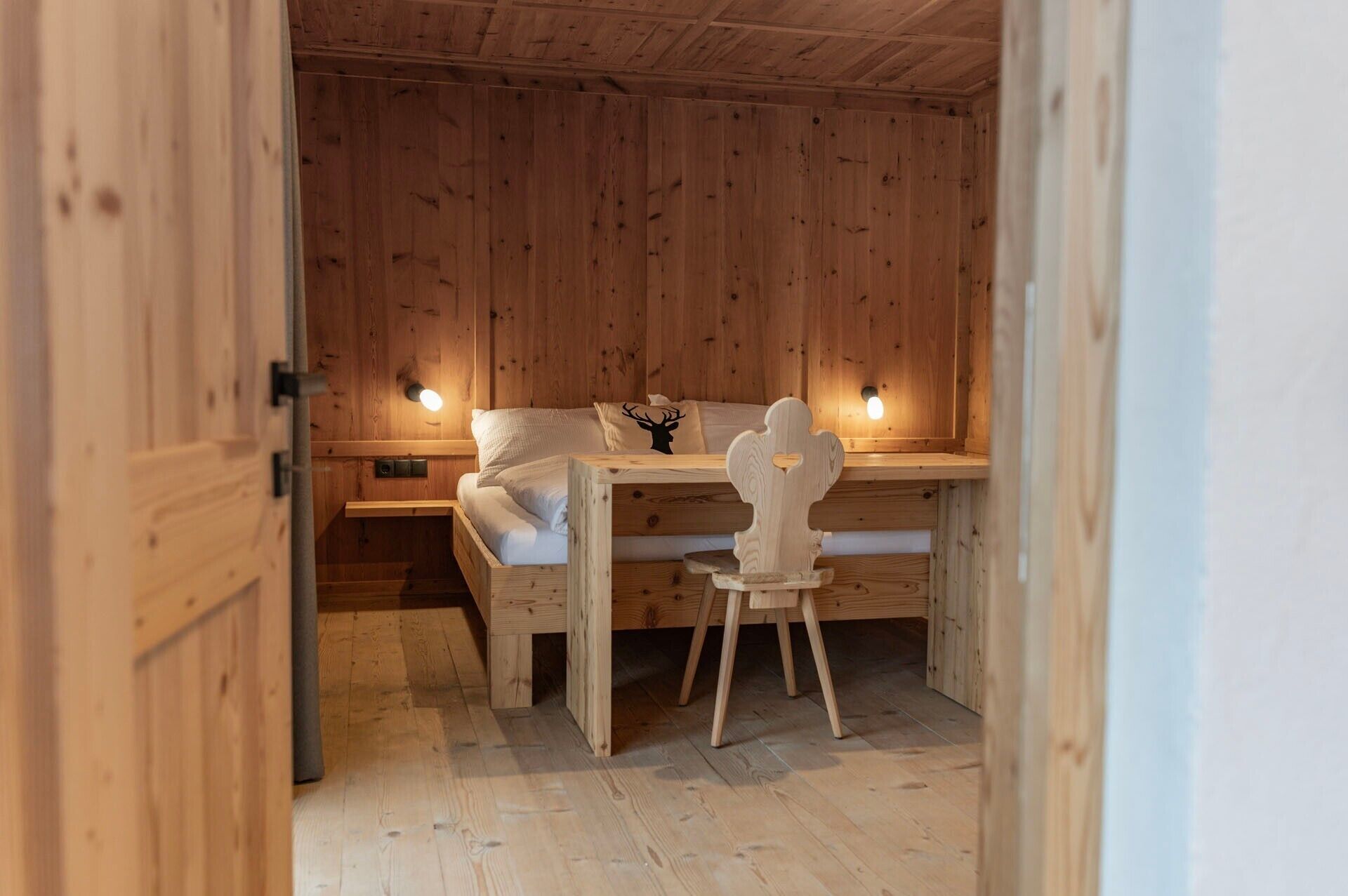 A wooden room with a bed, a desk, and a chair.