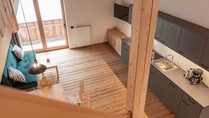 A modern kitchen with a built-in sink, a wooden dining table, and a teal sofa with patterned cushions. - Apartment 'Peunt' with Mountain View, Shared Terrace and Wi-Fi (Percha BZ)