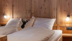A wooden-paneled room with a bed, two bedside lamps, and a pillow with a deer silhouette. - Apartment 'Peunt' with Mountain View, Shared Terrace and Wi-Fi (Percha BZ)