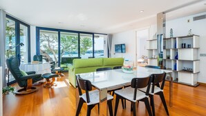En moderne stue med en grøn sofa, et glasbord og en hvid reol.
