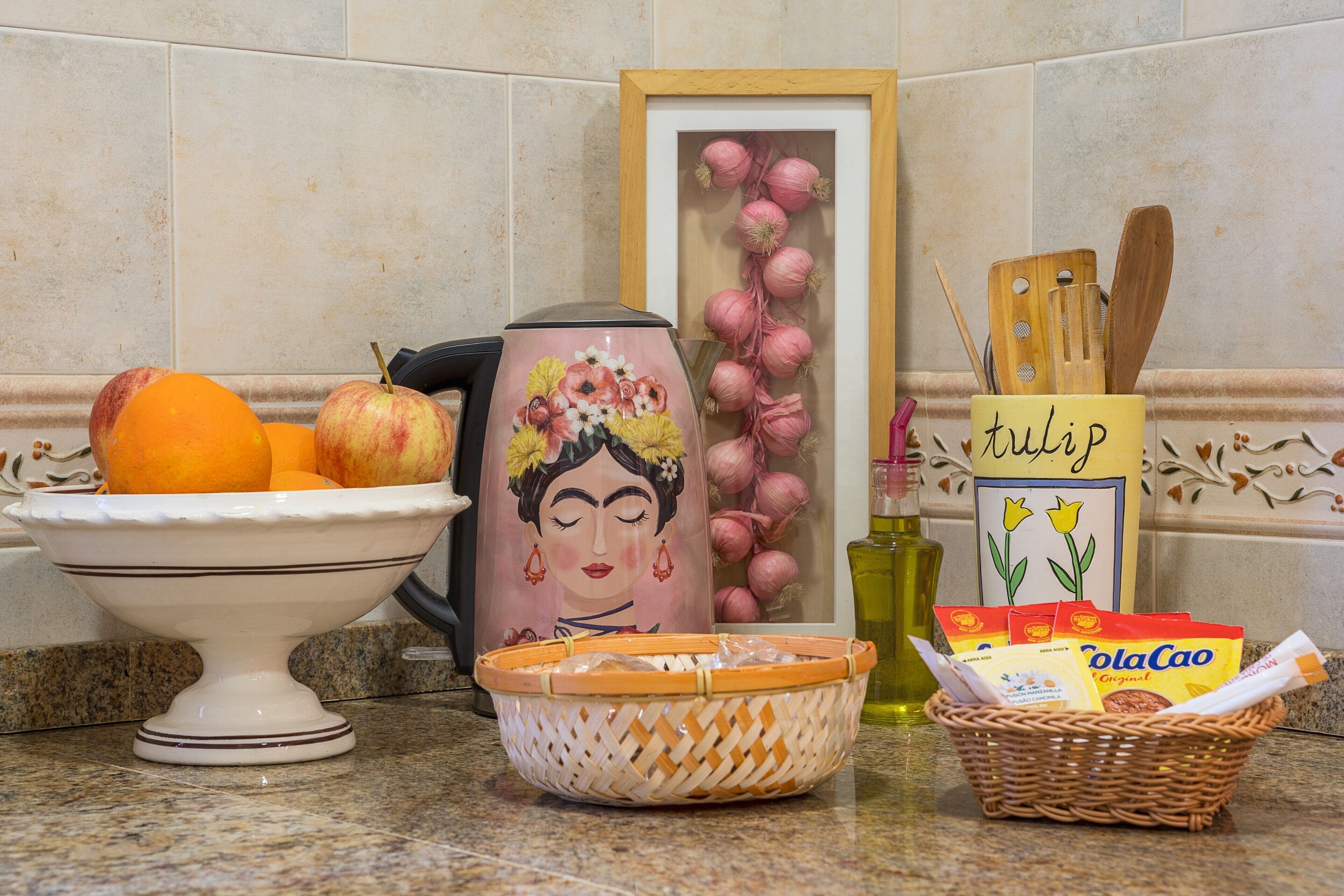 Una encimera de cocina con un frutero, una taza decorativa, una cesta y utensilios de cocina.