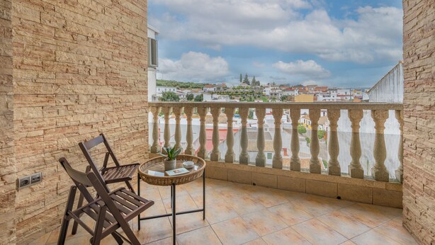 A balcony with a view of a town, a wicker table with a plant, and two wooden chairs. - Holiday Home 'León' with Private Terrace, Wi-Fi and Air Conditioning (Almodóvar del Río)