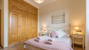 A bedroom with a large wooden wardrobe, a bed with pink linens, two bedside tables with lamps, and a motivational quote on the wall. - Holiday Home 'León' with Private Terrace, Wi-Fi and Air Conditioning (Almodóvar del Río)