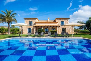 A pool with a checkered pattern, a stone building with balconies, and outdoor seating.