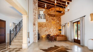 A spacious lobby with a stone wall, a chandelier, a leather rug, and a staircase. - Country House 'Fortuna' with Mountain View, Private Pool and Wi-Fi (Manacor)