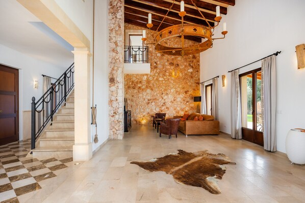 A spacious lobby with a stone wall, a chandelier, a leather rug, and a staircase.