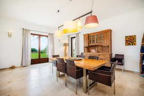 Un comedor con mesa y sillas de madera, una cocina con armarios de madera y vistas a través de puertas de vidrio.