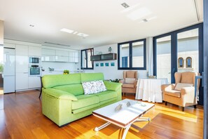Un soggiorno moderno con un divano verde, un tavolino bianco e una cucina sullo sfondo.