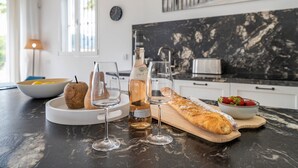 A kitchen with a marble countertop, a bottle of wine, glasses, a loaf of bread, and a bowl of strawberries.