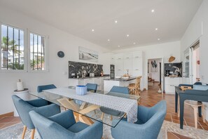 A modern kitchen with white cabinets, a marble backsplash, and a dining area with a glass table and blue chairs.