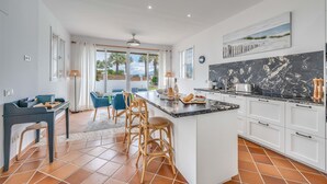 A modern kitchen with a large island, white cabinets, and a view of palm trees.