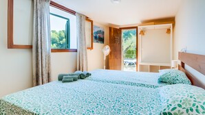 A bedroom with a bed, a window with curtains, a door leading to a balcony, and a wall-mounted fan. - Holiday Home 'Cala Deia' with Sea View, Wi-Fi and Air Conditioning (Illes Balears)