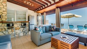 A cozy living area with a stone wall, a sofa, a wooden coffee table, and a balcony with chairs and an umbrella. - Holiday Home 'Cala Deia' with Sea View, Wi-Fi and Air Conditioning (Illes Balears)