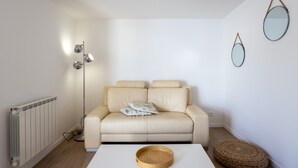 Un salon moderne avec un radiateur blanc, un canapé beige, un plateau rond en bois et une lampe sur pied.