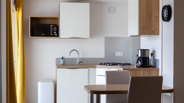 Une cuisine compacte équipée d’un four à micro-ondes, d’un évier et d’une cuisinière, ainsi qu’une table à manger avec des chaises et un rideau jaune.