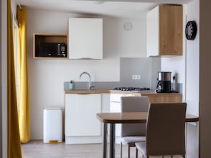 Une cuisine compacte équipée d’un four à micro-ondes, d’un évier et d’une cuisinière, ainsi qu’une table à manger avec des chaises et un rideau jaune.