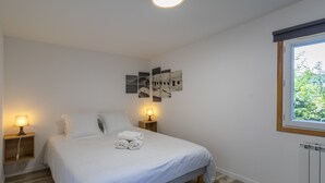 Une chambre à coucher avec un lit, deux lampes de chevet, une fenêtre et des œuvres d’art murales.